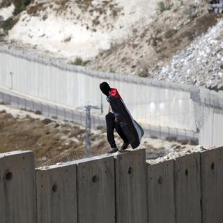 Un jeune portant le drapeau palestinien manifeste sur le mur de séparation à Abu Dis. [AP/Keystone - Mahmoud Illean]