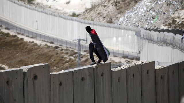 Un jeune portant le drapeau palestinien manifeste sur le mur de séparation à Abu Dis. [AP/Keystone - Mahmoud Illean]