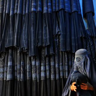 Une femme devant un magasin de burqa en Afghanistan. [Keystone - SAYED MUSTAFA]