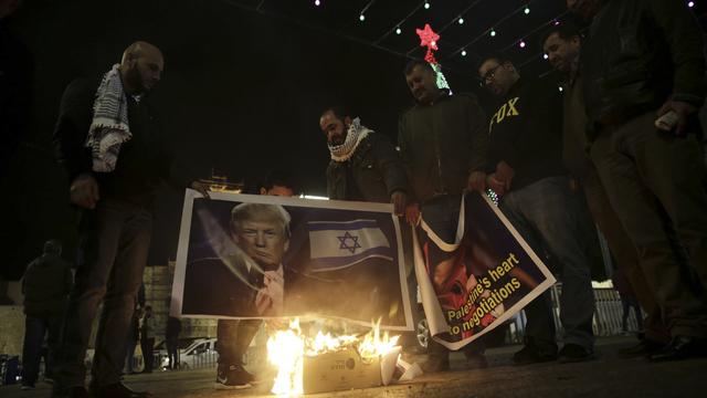 Des Palestiniens brûlent des affiches en protestation à la décision de Donald Trump de reconnaître Jérusalem comme capitale d'Israël. [Keystone - Mahmoud Illean]