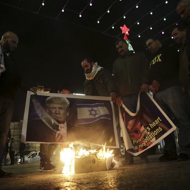 Des Palestiniens brûlent des affiches en protestation à la décision de Donald Trump de reconnaître Jérusalem comme capitale d'Israël. [Keystone - Mahmoud Illean]