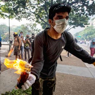 Un manifestant s'apprête à lancer un cocktail Molotov à Caracas. [Keystone - EPA/MIGUEL GUTIERREZ]