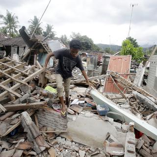 Un homme marche parmi les débris causés par le séisme dans l'ouest de l'île indonésienne de Lombok. [AP Photo - Firdia Linsawati]