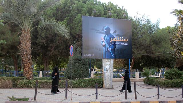 Deux femmes en niqab, sous un panneau de propagande du groupe Etat islamique, dans une rue de Raqqa en novembre 2014. [AFP - Raqa Media Center]