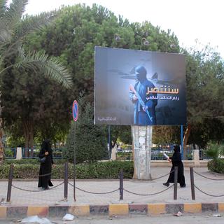 Deux femmes en niqab, sous un panneau de propagande du groupe Etat islamique, dans une rue de Raqqa en novembre 2014. [AFP - Raqa Media Center]