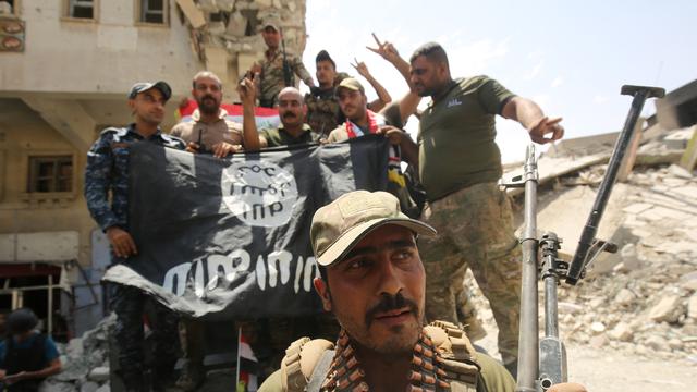 Des membres des forces irakiennes posant devant un drapeau de l'EI lors de la libération de Mossoul, à l'été 2017. [AFP - Ahmad Al-Rubaye]