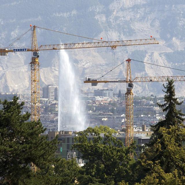 Deux grues travaillent sur un chantier pour la construction d'un immeuble avec comme fond le jet d'eau, ce lundi 22 aout 2011 a Geneve. (KEYSTONE/Salvatore Di Nolfi) [Keystone - Salvatore Di Nolfi]