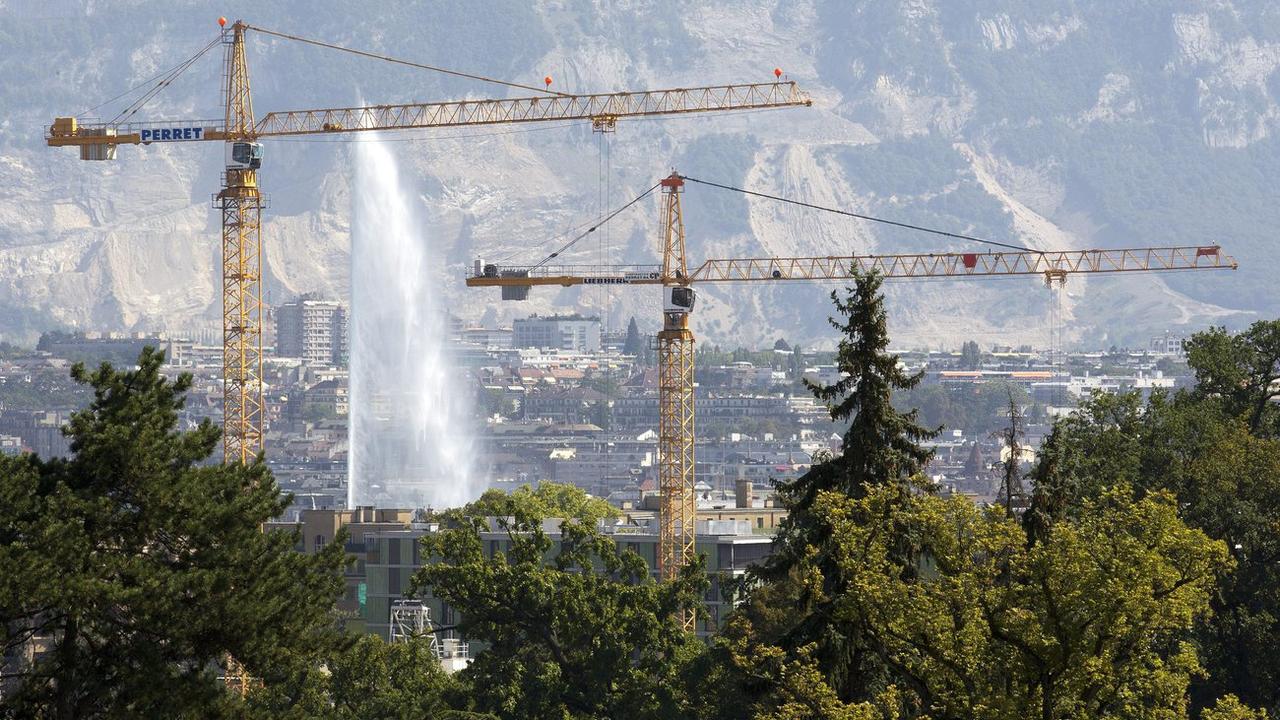 Deux grues travaillent sur un chantier pour la construction d'un immeuble avec comme fond le jet d'eau, ce lundi 22 aout 2011 a Geneve. (KEYSTONE/Salvatore Di Nolfi) [Keystone - Salvatore Di Nolfi]