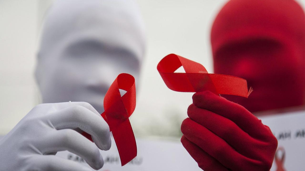 Deux personnes masquées brandissent les rubans rouges, signe de solidarité envers les victimes du VIH et du sida. [Keystone - EPA/FULLY HANDOKO]