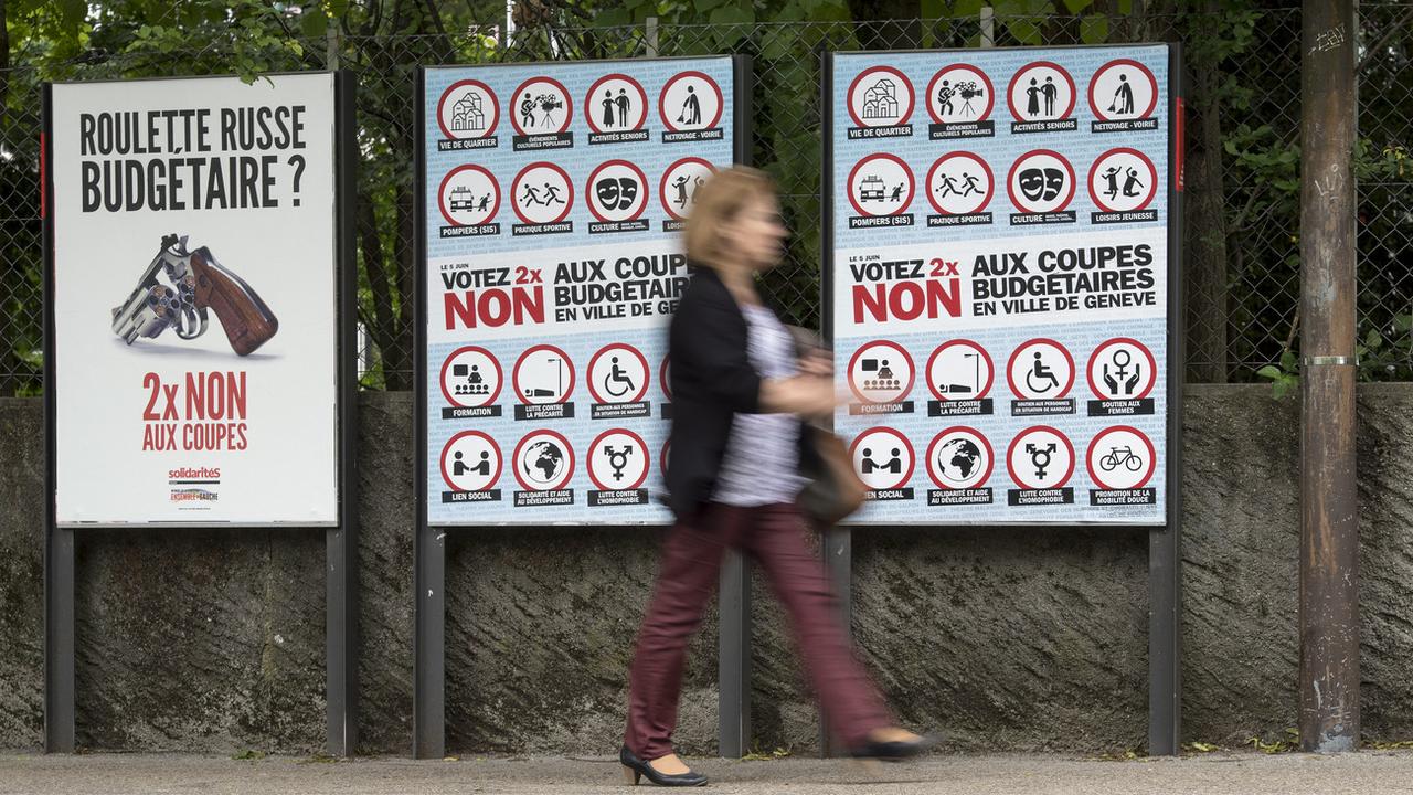 Une passante devant les affiches de la votation annulée sur les coupes budgétaires en Ville de  Genève. [Keystone - Martial Trezzini]