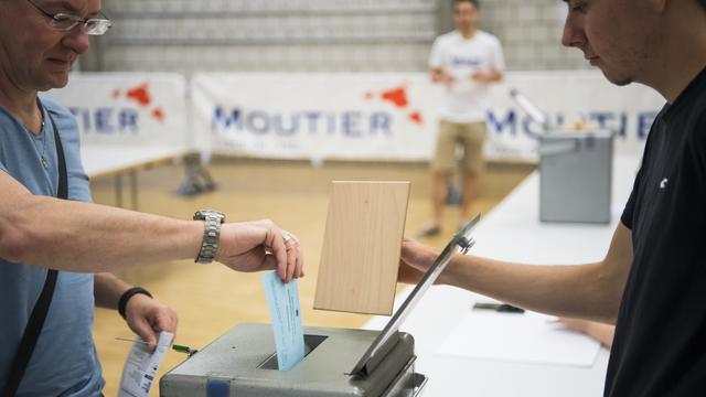 Un habitant de Moutier en train de glisser son bulletin dans l'urne pour le vote du 18 juin 2017. [Keystone - Jean-Christophe Bott]