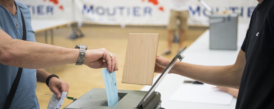 Un habitant de Moutier en train de glisser son bulletin dans l'urne pour le vote du 18 juin 2017. [Keystone - Jean-Christophe Bott]