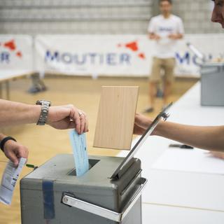 Un habitant de Moutier en train de glisser son bulletin dans l'urne pour le vote du 18 juin 2017. [Keystone - Jean-Christophe Bott]