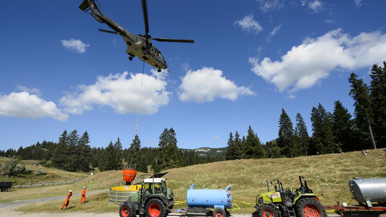 Un hélicoptère Super Puma de l'armée suisse apporte de l'eau dans un réservoir pour abreuver les vaches d'un paysan dans la région du Marchairuz. (image d'archives de la canicule de 2015) [Keystone - Jean-Christophe Bott]