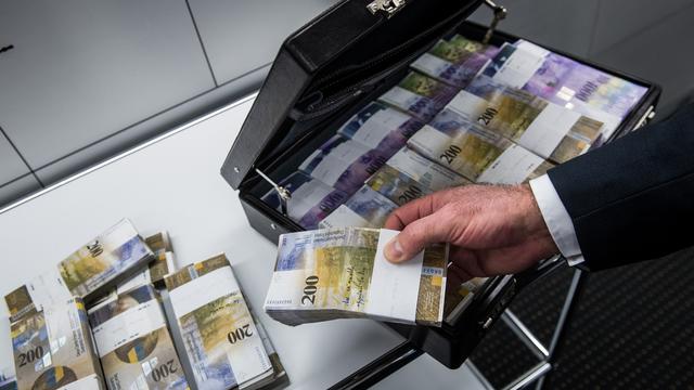 Un homme remplissant une valise de billets de 200 francs (image d'illustration). [Keystone - Gabriele Putzu]