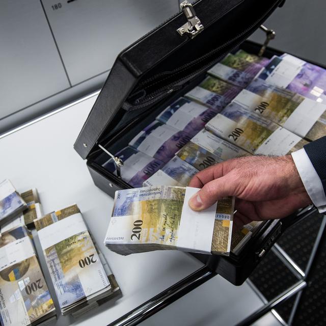 Un homme remplissant une valise de billets de 200 francs (image d'illustration). [Keystone - Gabriele Putzu]