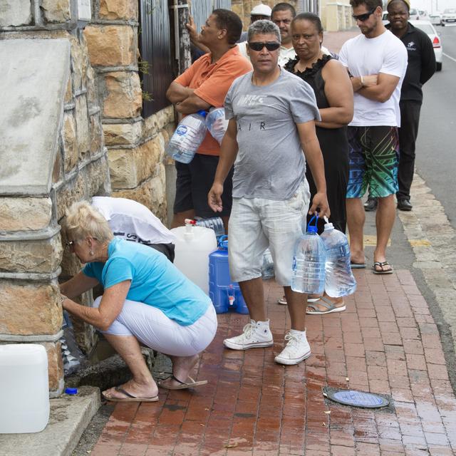 People collect drinking water from pipes fed by an underground spring, in St. James, about 25km from the city centre, on January 19, 2018, in Cape Town. Cape Town will next month slash its individual daily water consumption limit by 40 percent to 50 litres, the mayor said on January 18, as the city battles its worst drought in a century. [AFP - Rodger Bosch]