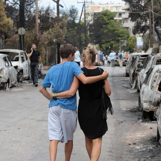 Deux habitants de Mati, près d'Athènes, marchent dans une rue ravagée par un incendie meurtrier. [EPA/Keystone - Pantelis Saitas]
