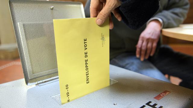 Une personne dépose son bulletin de vote dans une urne. [Keystone - Laurent Gillieron]