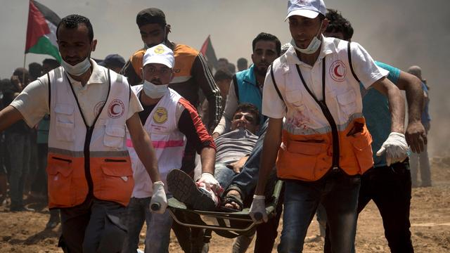 Des médecins portent un homme blessé par balle durant une manifestation à la frontière de Gaza, lundi 14 mai, jour de l'inauguration de l'ambassade américaine à Jérusalem. [keystone - LUCA PIERGIOVANNI]