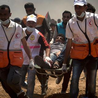 Des médecins portent un homme blessé par balle durant une manifestation à la frontière de Gaza, lundi 14 mai, jour de l'inauguration de l'ambassade américaine à Jérusalem. [keystone - LUCA PIERGIOVANNI]