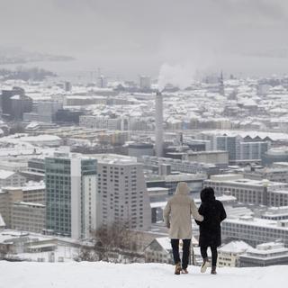 Un couple marche dans la neige sur les hauteurs de la ville de Zurich. [Keystone - Ennio Leanza]