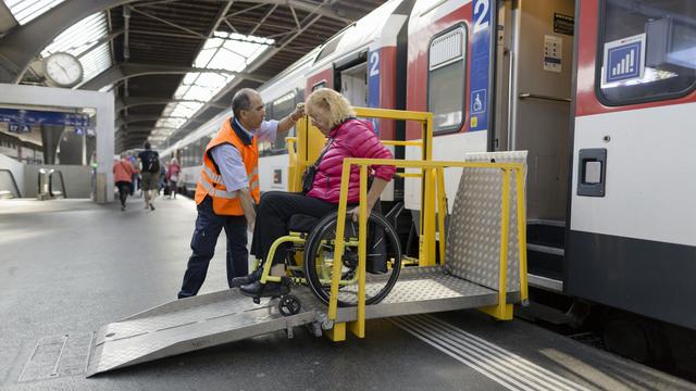 Un employé des CFF aide une personne en chaise roulante à grimper dans le train. [Keystone - Gaëtan Bally]