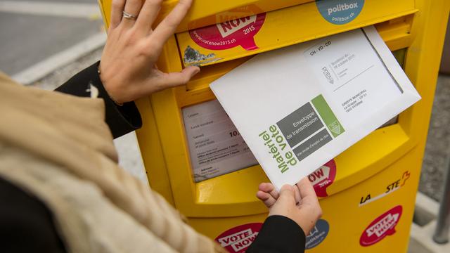 Une personne glisse un bulletin de vote dans une boite aux lettres lors de l'opération "Easyvote" pour inciter les jeunes à voter en 2015. [Keystone - Jean-Christophe Bott]