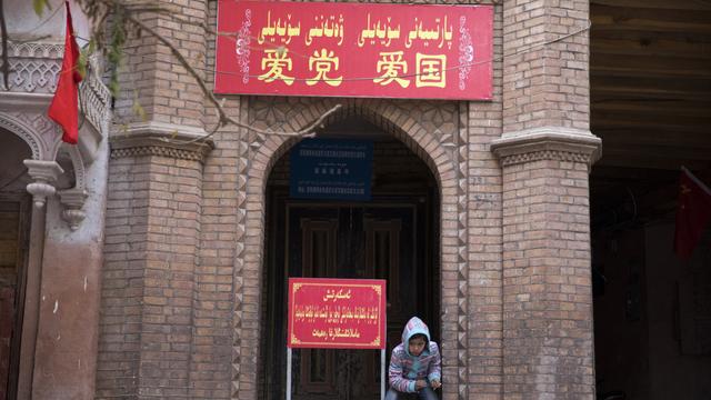 Un enfant se repose près de l'entrée d'une mosquée dans l'ouest de la Chine. Sur la pancarte, on peut lire "Aimez le parti, aimez le pays". [AP - NG HAN GUAN]