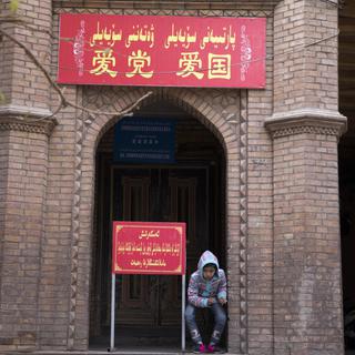 Un enfant se repose près de l'entrée d'une mosquée dans l'ouest de la Chine. Sur la pancarte, on peut lire "Aimez le parti, aimez le pays". [AP - NG HAN GUAN]