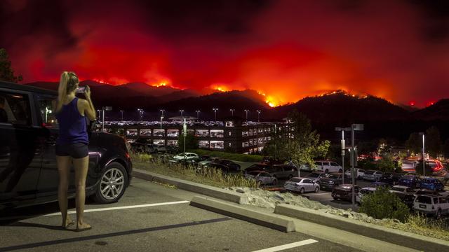 Une habitante de Cache Creek filmant les incendies au loin depuis un parking. [Keystone - Peter Da Silva]