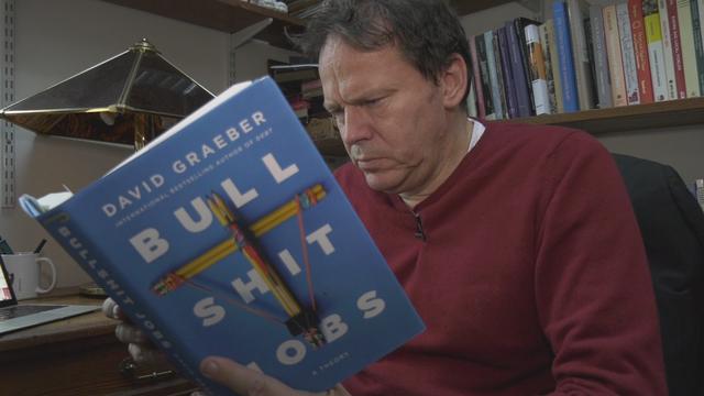 David Graeber, auteur du livre "Bullshit Jobs", qu'il tient dans ses mains. [RTS]