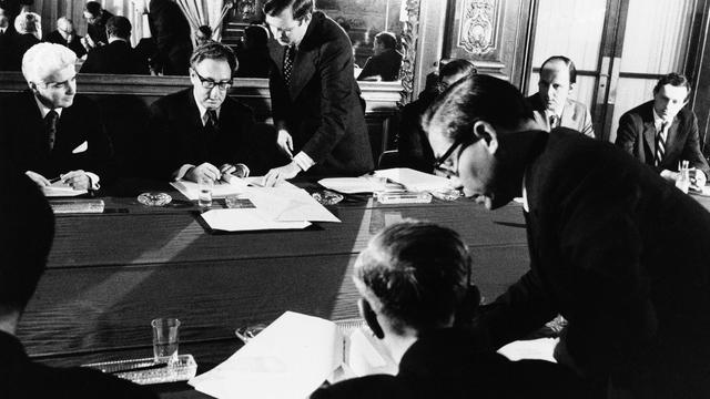 Henry Kissinger (assis, de face) et Le Duc Tho, membre du politburo nord-vietnamien (au premier plan, de dos) se font face lors de la signature du traité de paix entre leurs deux pays, à Paris, le 24 janvier 1973. Ils seront récompensés, cette année-là, par le prix Nobel de la Paix. [AP Photo/White House; KEYSTONE/White House]