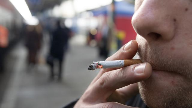 Un homme fume sur le quai d'une gare en Suisse romande. [Keystone - Martin Ruetschi]