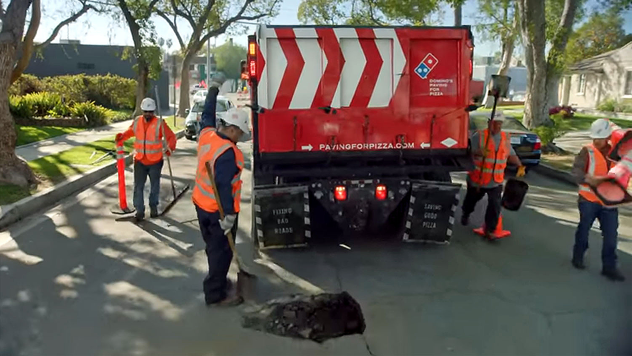 Une équipe mandatée par la chaîne de pizzas rebouche un trou dans l'asphalte. [YouTube]
