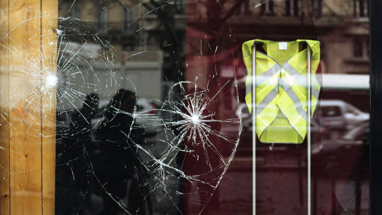 Une vitrine brisée affichant un gilet jaune, en soutien au mouvement de contestation. [AP Photo / Keystone - Kamil Zihnioglu]