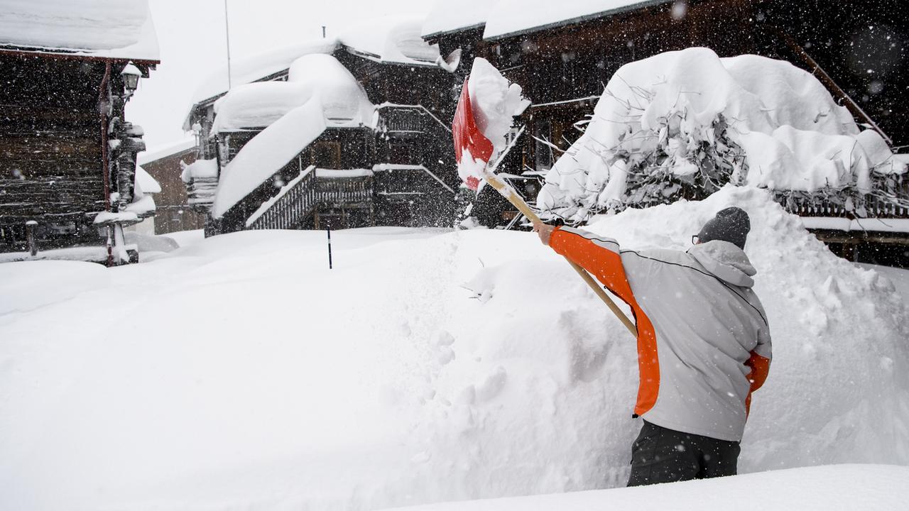 Une personne déblaie de la neige dimanche à Bellwald dans la Vallée de Conches en Valais. [Keystone - Jean-Christophe Bott]