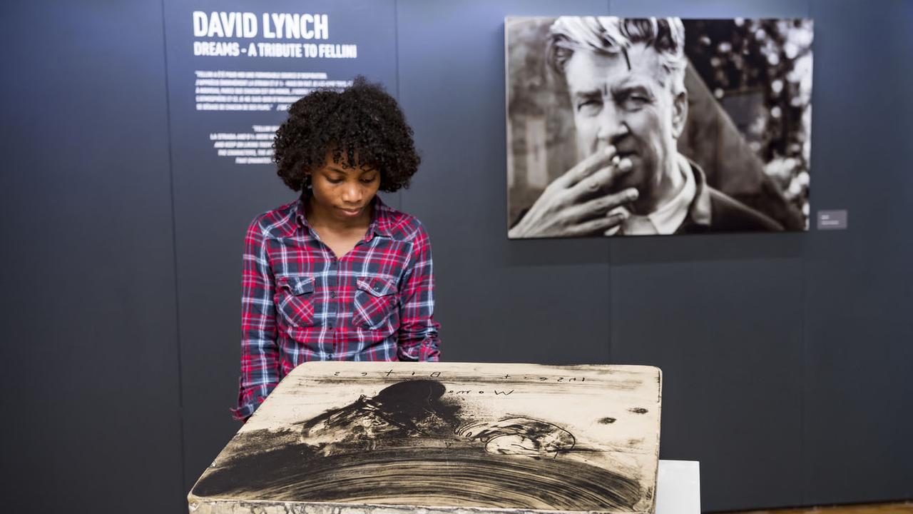 Une femme regarde une lithographie du cinéaste David Lynch lors de l'exposition "David Lynch, Dreams - A tibute to Fellini" à la Maison du Diable à Sion. [Keystone - Jean-Christophe Bott]