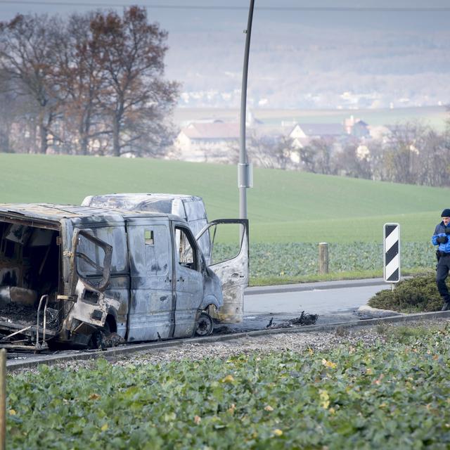 Mardi 3 décembre: des policiers observent le fourgon de transports de fonds attaqué durant la nuit à Daillens (VD) avant d'être incendié. [Keystone - Laurent Gillieron]