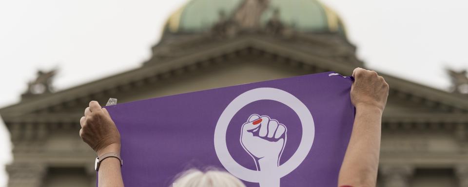 Une manifestante de de la grève des femmes brandit un drapeau devant le Palais fédéral à Berne. [Keystone - Alessandro della Valle]