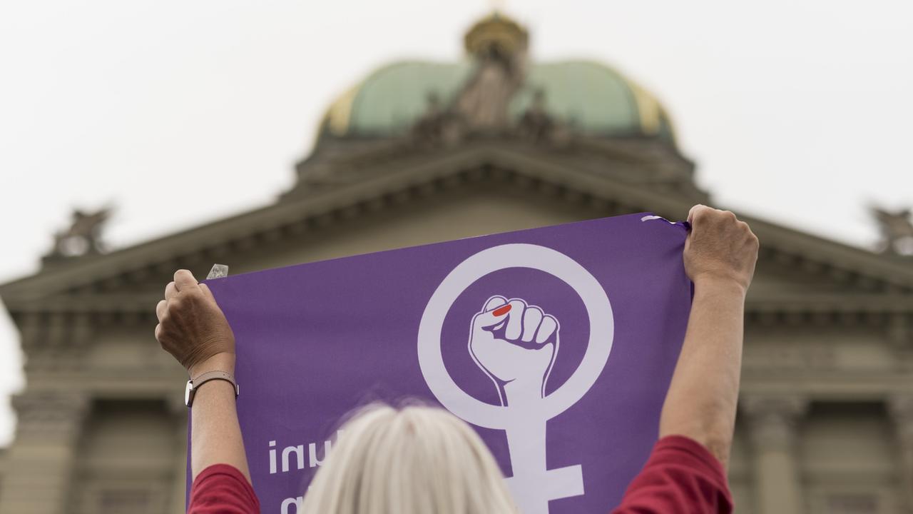Une manifestante de de la grève des femmes brandit un drapeau devant le Palais fédéral à Berne. [Keystone - Alessandro della Valle]
