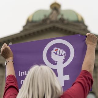Une manifestante de de la grève des femmes brandit un drapeau devant le Palais fédéral à Berne. [Keystone - Alessandro della Valle]