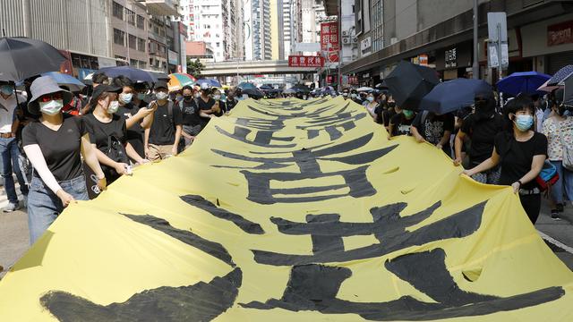 Des manifestants à Hong Kong défilent masqués en tentant une banderole "Que la gloire soit à Hong Kong". [Keystone/AP Photo - Vincent Thian]