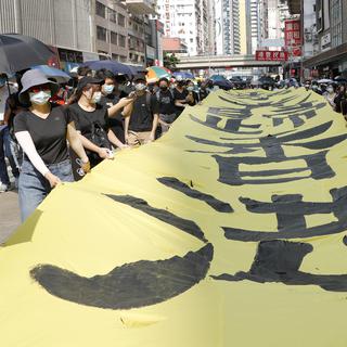 Des manifestants à Hong Kong défilent masqués en tentant une banderole "Que la gloire soit à Hong Kong". [Keystone/AP Photo - Vincent Thian]