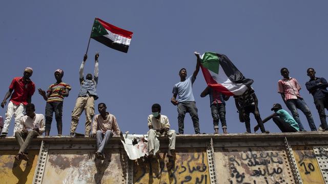 Des manifestants brandissent le drapeau soudanais devant le quartier général de l'armée à Khartoum. [Keystone/AP - Salih Basheer]