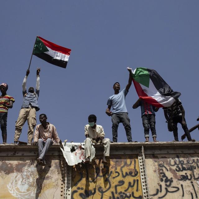 Des manifestants brandissent le drapeau soudanais devant le quartier général de l'armée à Khartoum. [Keystone/AP - Salih Basheer]