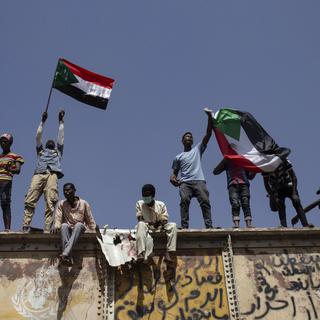 Des manifestants brandissent le drapeau soudanais devant le quartier général de l'armée à Khartoum. [Keystone/AP - Salih Basheer]