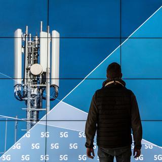 Un homme se tient devant un écran affichant une antenne 5G. [Keystone - Boris Roessler]