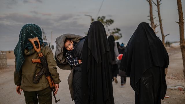 Des femmes, veuves du groupe Etat islamique, marchent dans le camp de Al-Hol sous la surveillance d'une combattante kurde. [AFP - Bulent Kilic]