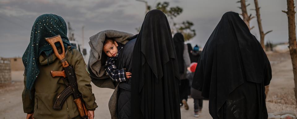 Des femmes, veuves du groupe Etat islamique, marchent dans le camp de Al-Hol sous la surveillance d'une combattante kurde. [AFP - Bulent Kilic]